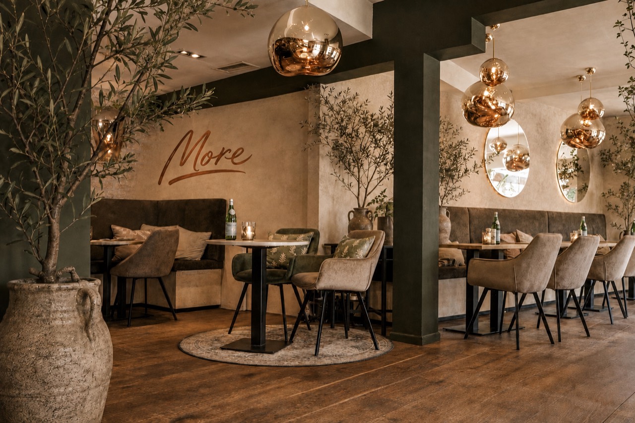 Tafels en warm verlichte inrichting met het MORE-logo
